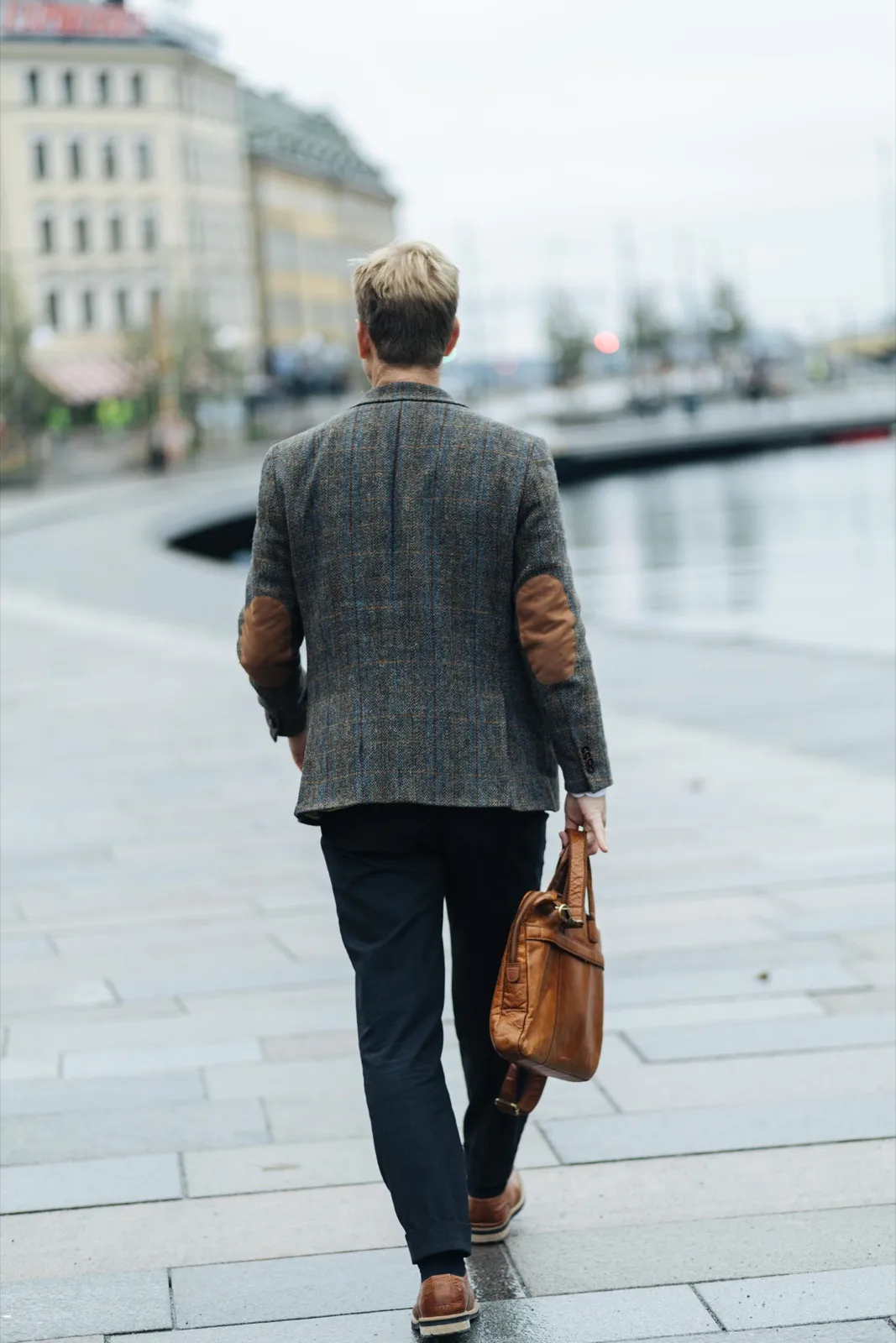 A man in a jacket walking alone along the quay with a briefcase.