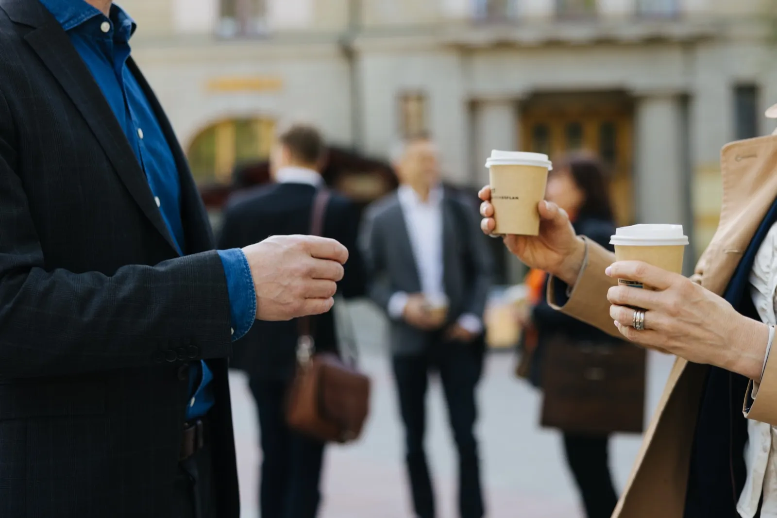 Two people with coffee talking on the street.