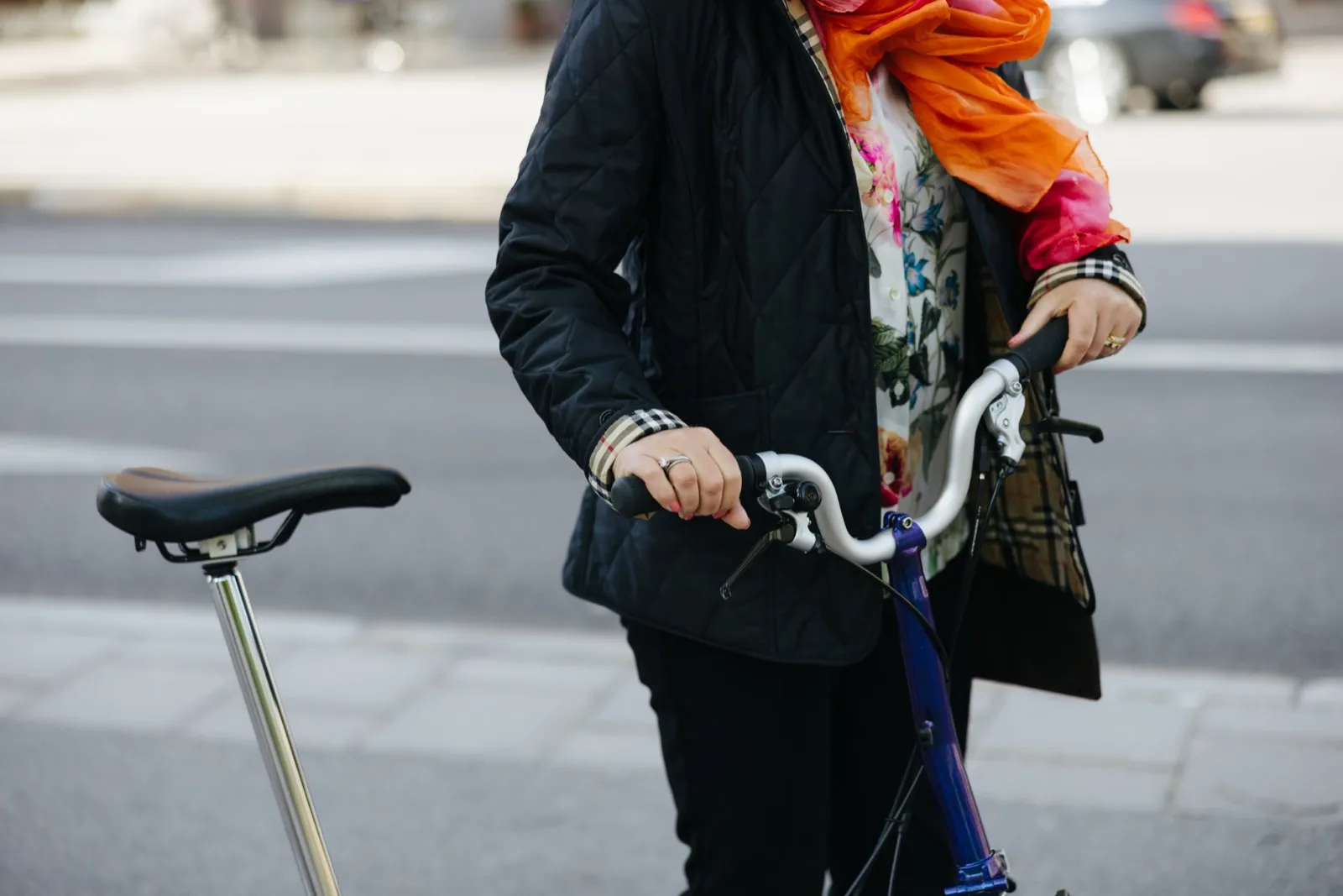 A person in a jacket and a colorful scarf walking a bicycle down the street.