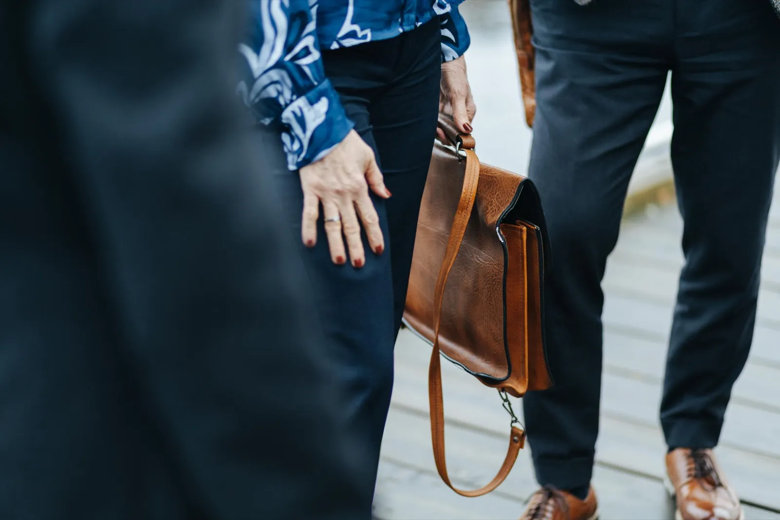 Hands and a leather briefcase, three people walking together along a pier.
