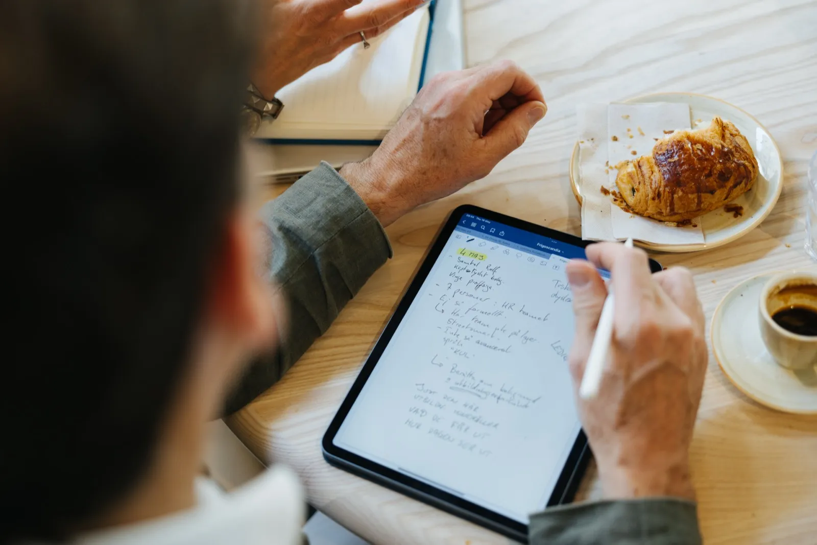 Notes on a tablet at a café table, seen over the shoulder.
